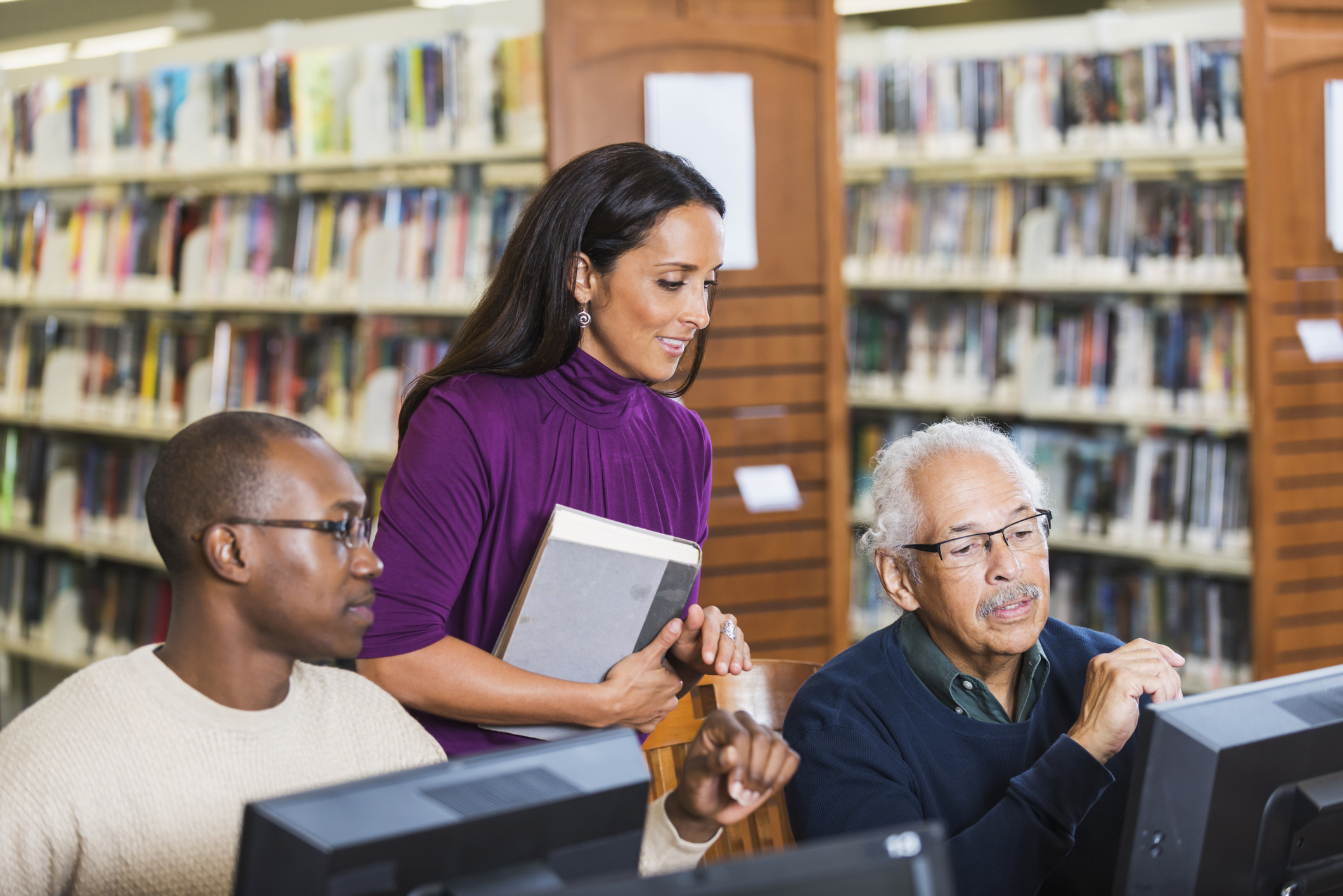 People helping senior man use computer in library